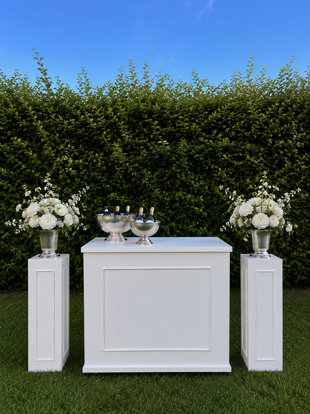 Hvit bar med blomster og champagnekjølere mot hekk